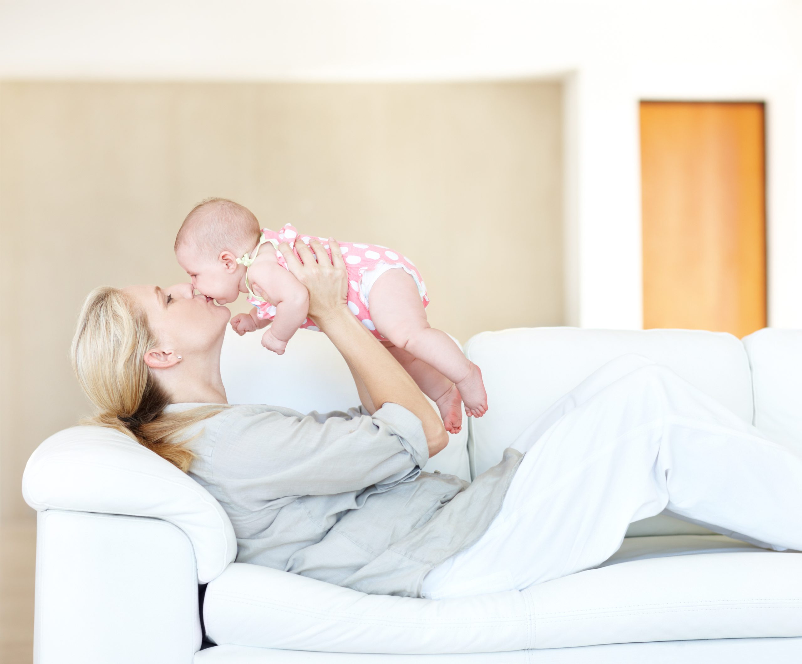 You're my little angel! Thankful mother giving her cherubic newborn a loving kiss upon the lips relaxing on sofa
